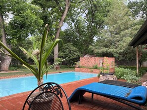 Una piscina con una colchoneta azul, un muro de ladrillo y un árbol al fondo.