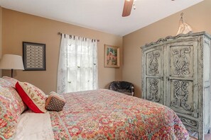 Ein Schlafzimmer mit einem Bett, einem Sessel, einem Kleiderschrank und einem Deckenventilator.