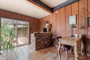 Een kamer met houten wanden, een metselstenen open haard, een eettafel met stoelen en een groot raam.