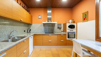 Una cocina con encimeras de granito, armarios de madera, campana extractora de acero inoxidable, horno empotrado y una silla blanca.