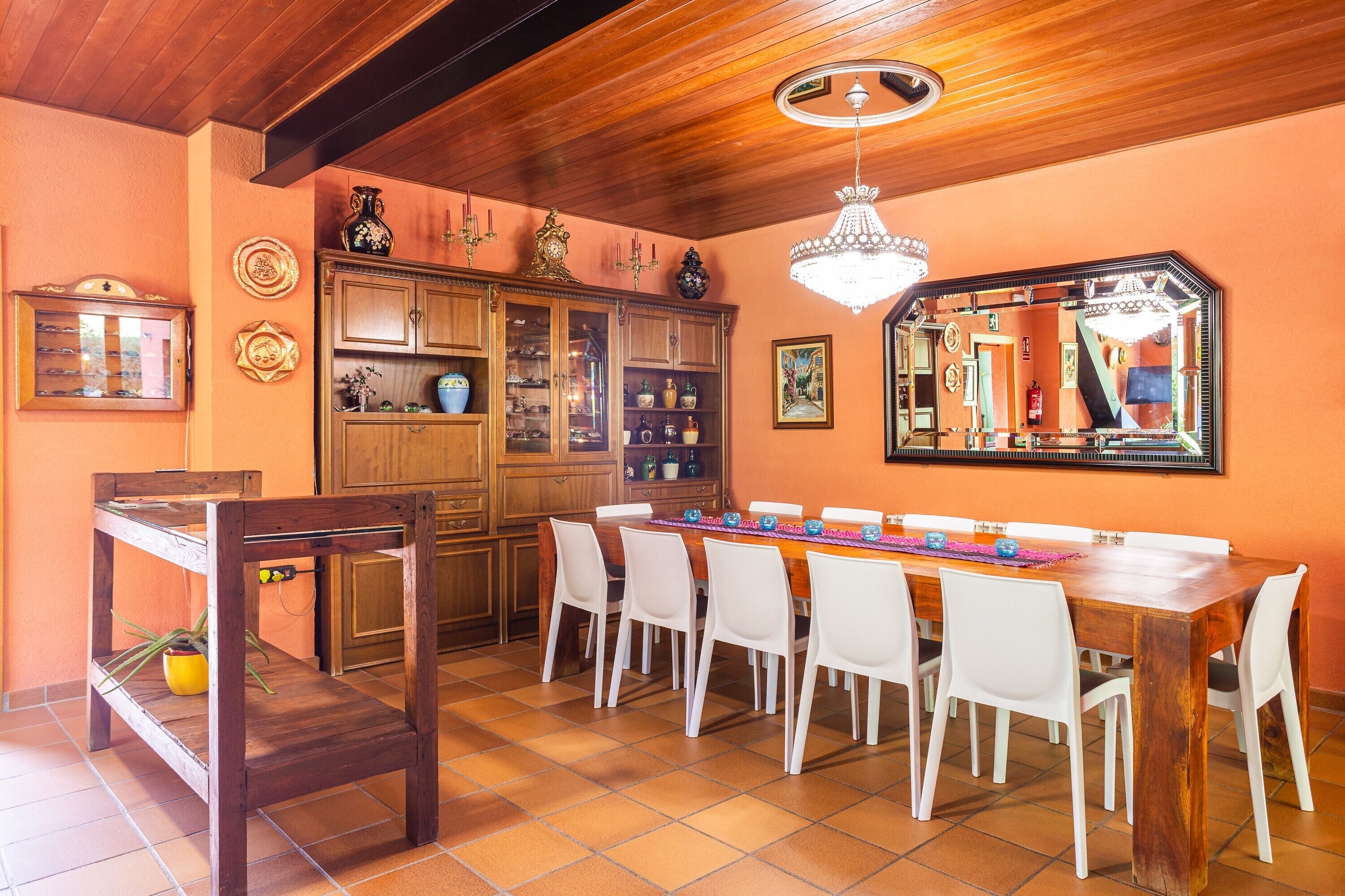Comedor con mesa de madera, sillas blancas, candelabro y un espejo grande.
