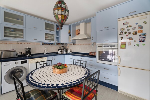 A kitchen with a round table, chairs, a washing machine, and a refrigerator.