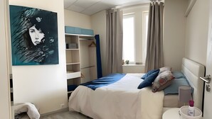 Une chambre à coucher avec un lit, une table de chevet, une fenêtre avec des rideaux, une armoire et un tableau au mur.