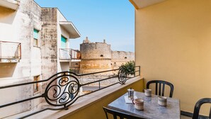 A balcony with a table and chairs, a view of a historic stone building, and a metal railing.