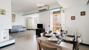 A dining area with a table set for two, a sofa, a TV, and a kitchen visible in the background.