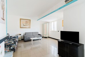 A modern living room with a sofa, a coffee table, a TV on a cabinet, and a painting on the wall.