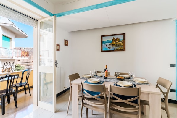 A dining area with a table set for four, chairs, a painting on the wall, and a view of a building outside.