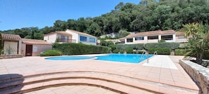 A pool area with two swimming pools, surrounded by buildings with tiled roofs and a hilly backdrop.