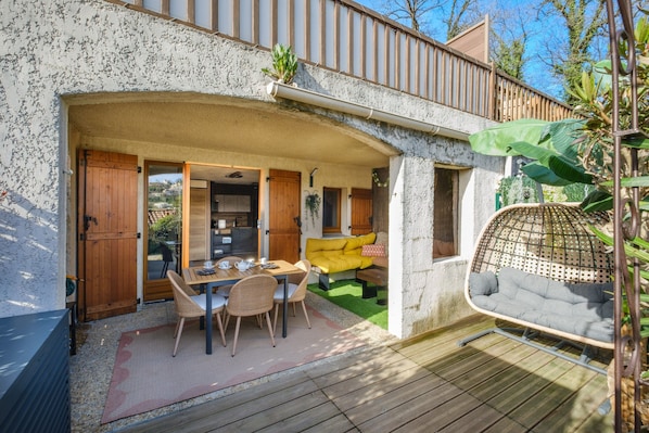 A covered outdoor dining area with a table and chairs, a yellow sofa, and a hanging chair.