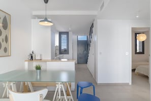 A modern kitchen with a glass dining table, a blue chair, and pendant lighting.