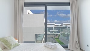 A modern hotel room with a large bed, a view of the city through floor-to-ceiling windows, and a balcony with a glass railing. - Apartment 'Palacio De Pilas 22' with Shared Pool, Wi-Fi and Air Conditioning (Zahara de los Atunes)