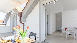 A modern apartment with a dining area featuring a wooden table and chairs, a vase with flowers, and a view of the adjacent living space. - Palmaiola by Interhome (Follonica)