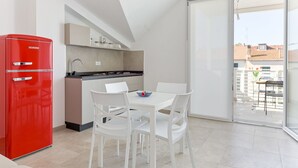 A modern kitchen with a red refrigerator, white dining chairs, and a large sliding glass door leading to a balcony. - Palmaiola by Interhome (Follonica)