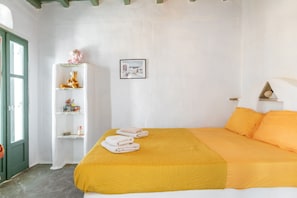 Quarto com cama, prateleira com objetos decorativos, quadro emoldurado e porta verde.