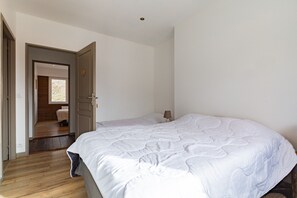 A bedroom with a large bed, a door leading to a wooden room, and a small bedside table with a lamp. - Holiday Home 'La Clé du Vercors' with Panoramic Alpine Views (Presles)