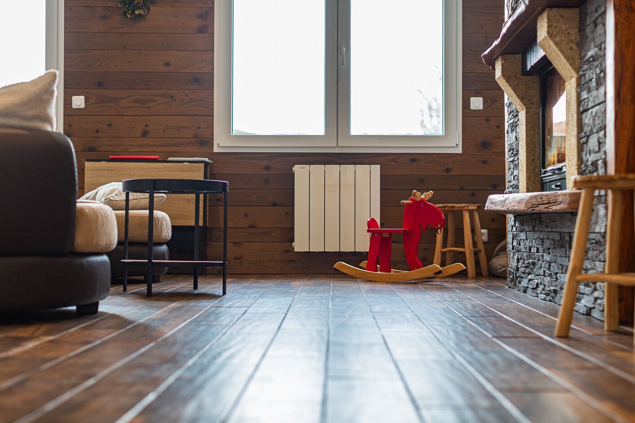 A cozy room with wooden flooring, a rocking chair, a chair, a table, and a fireplace.