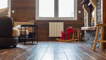 A cozy room with wooden flooring, a rocking chair, a chair, a table, and a fireplace.