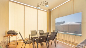 Comedor con mesa y sillas, una parrilla y un ventanal con vistas a edificios.