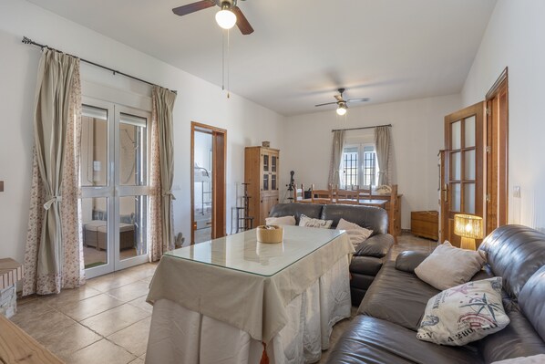 A spacious living area with a glass-top table, leather sofa, and ceiling fans.