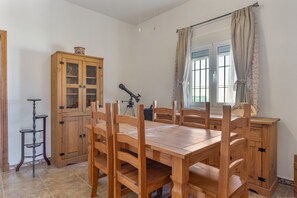 A wooden dining table with chairs, a cabinet with glass doors, a tripod, and a window with curtains.