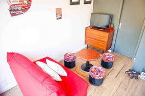 Un sofá rojo con almohadones, un mueble de televisión de madera con un televisor de pantalla plana, y tres otomanas coloridas.