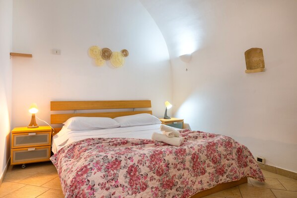 A bedroom with a bed, two bedside tables with lamps, a wall-mounted light fixture, and a decorative wall piece.