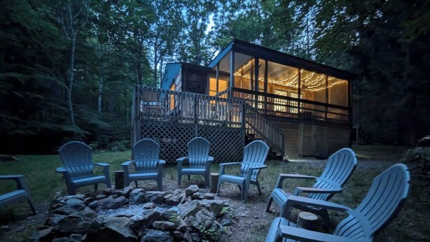 A cabin with a deck and a fire pit with chairs.