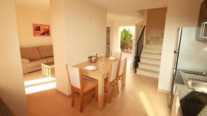 A dining area with a table set for four, a sofa, and a staircase leading to another level. - Holiday Home 'Residence Club El Paraiso 30' with Sea View, Wi-Fi and Air Conditioning (Sa Ràpita)