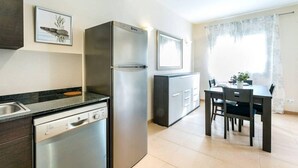 Une cuisine compacte équipée d’un lave-vaisselle, d’un réfrigérateur, d’une table à manger avec des chaises et d’une fenêtre avec des rideaux.