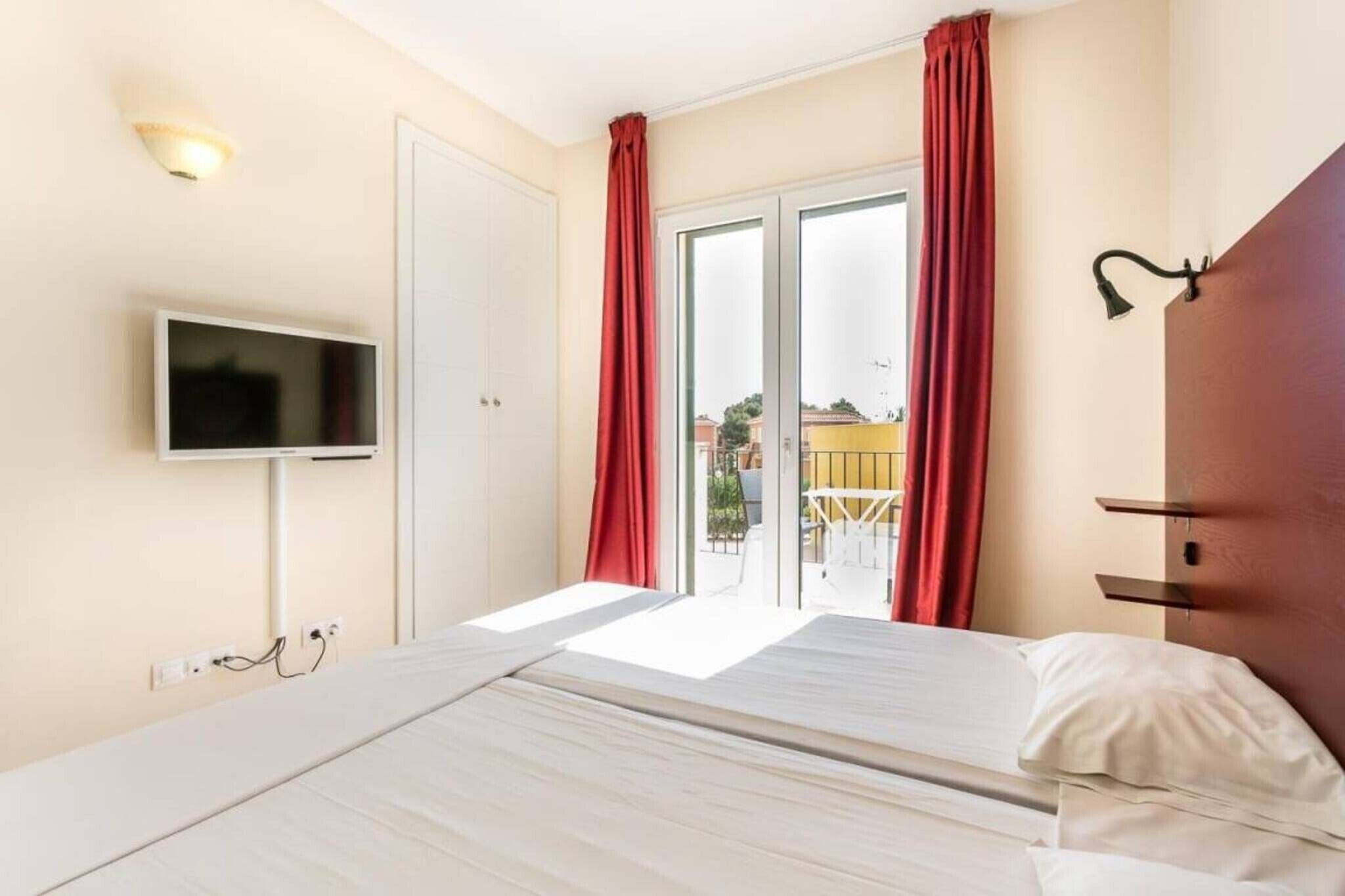 A hotel room with a bed, a TV, a sliding glass door, and a red curtain.