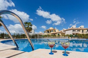 A swimming pool with two drinks on the edge, surrounded by a clear blue sky and a large building in the background.