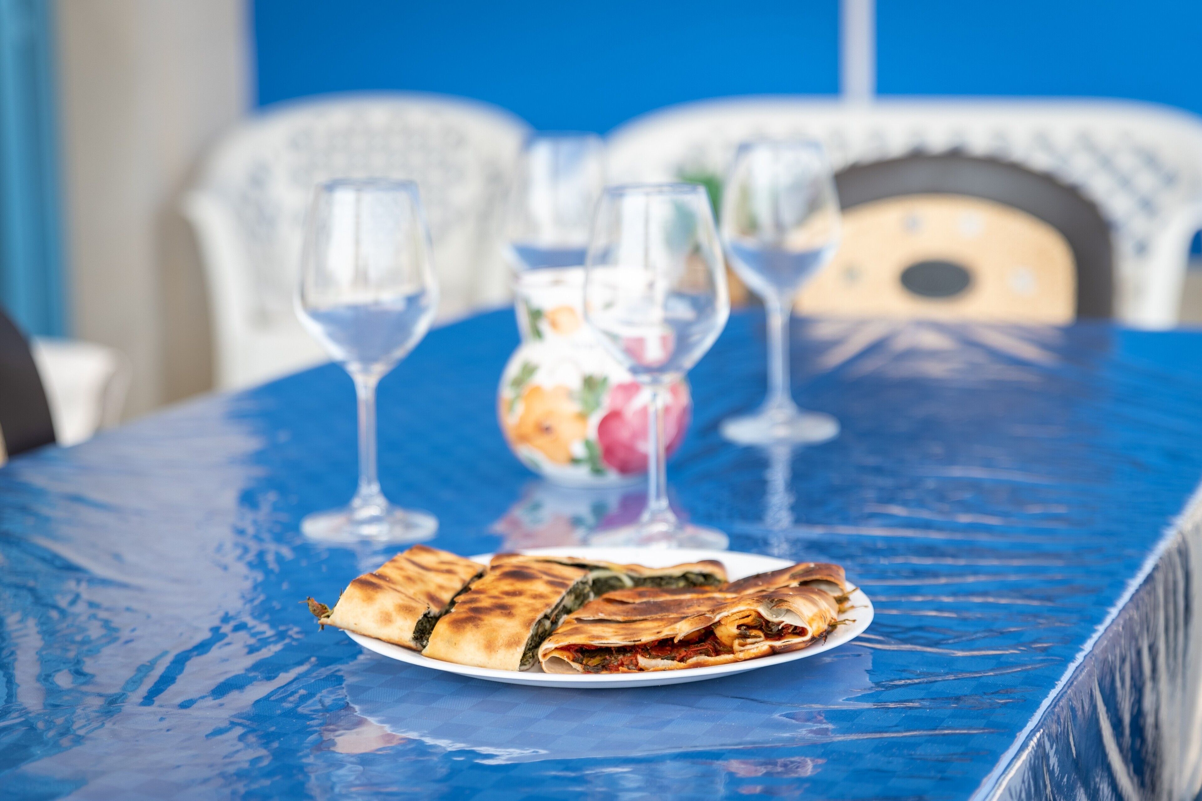 Une table à manger avec une assiette de nourriture, deux verres à vin et un vase rempli de fleurs.