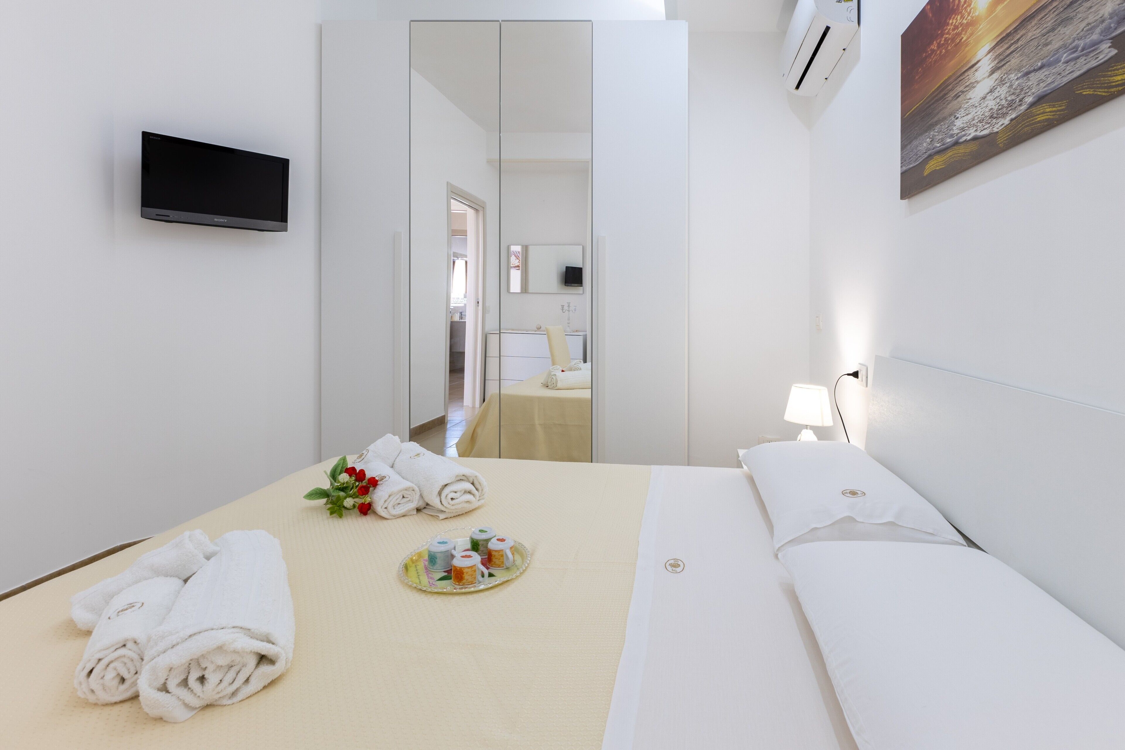 Ein Hotelzimmer mit Bett, Fernseher, Spiegel und einem Bild an der Wand.