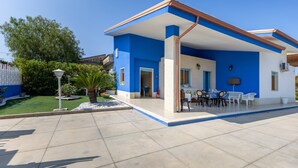 Une maison moderne à l’extérieur bleu, dotée d’un patio couvert et d’un jardin bien entretenu.