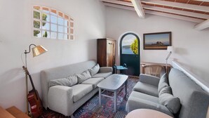 A living room with a sofa, a small table, a lamp, a guitar, and a view through a door.