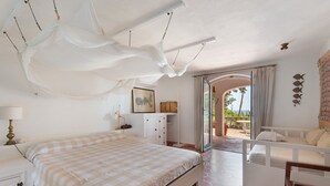 A bedroom with a bed, a desk, a chair, and a view of the outdoors.