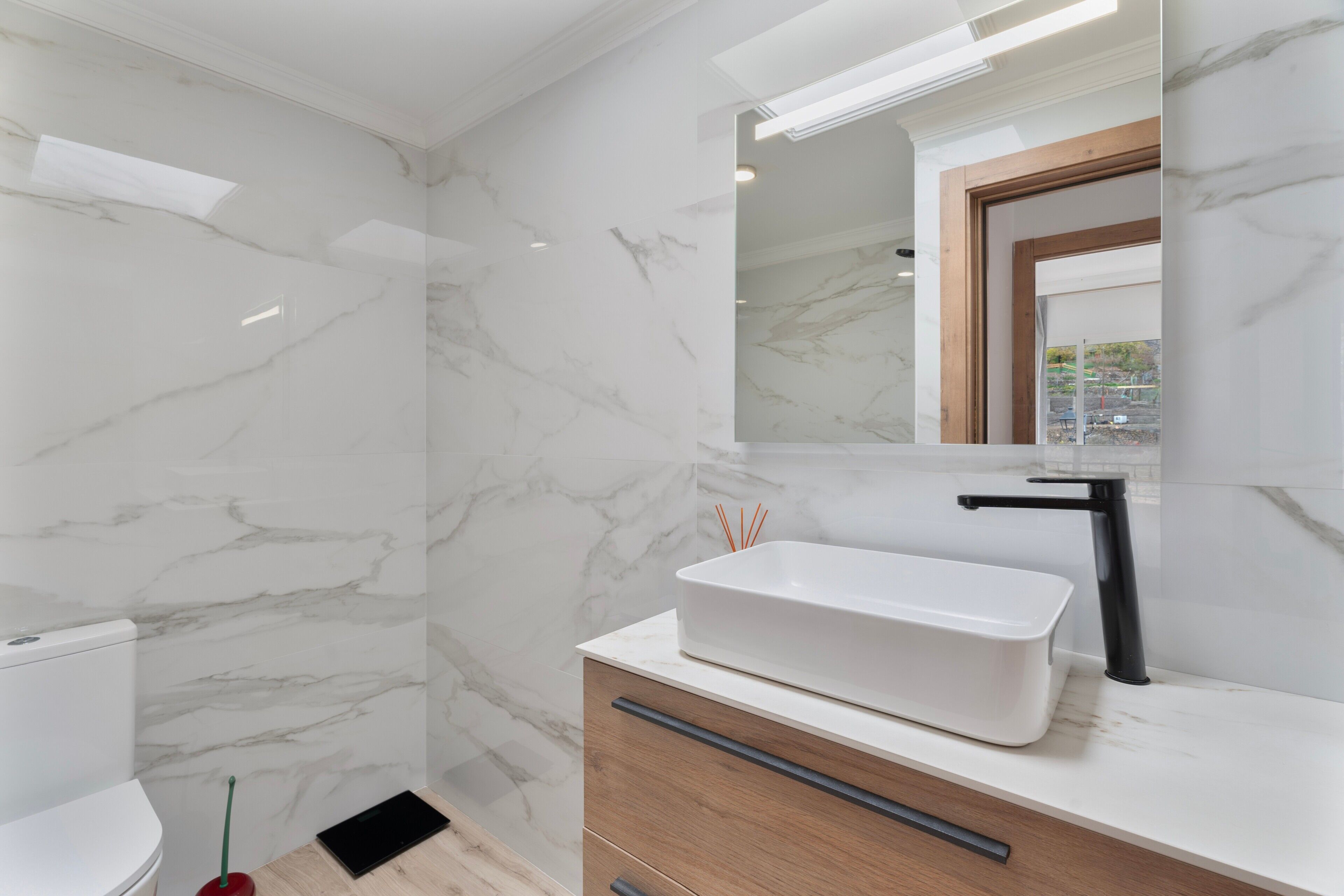 Un baño con paredes de mármol, un lavamanos blanco y un tocador de madera.