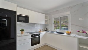 A modern kitchen with white cabinets, a black refrigerator, a microwave, an oven, a sink, and a window with a view of greenery.