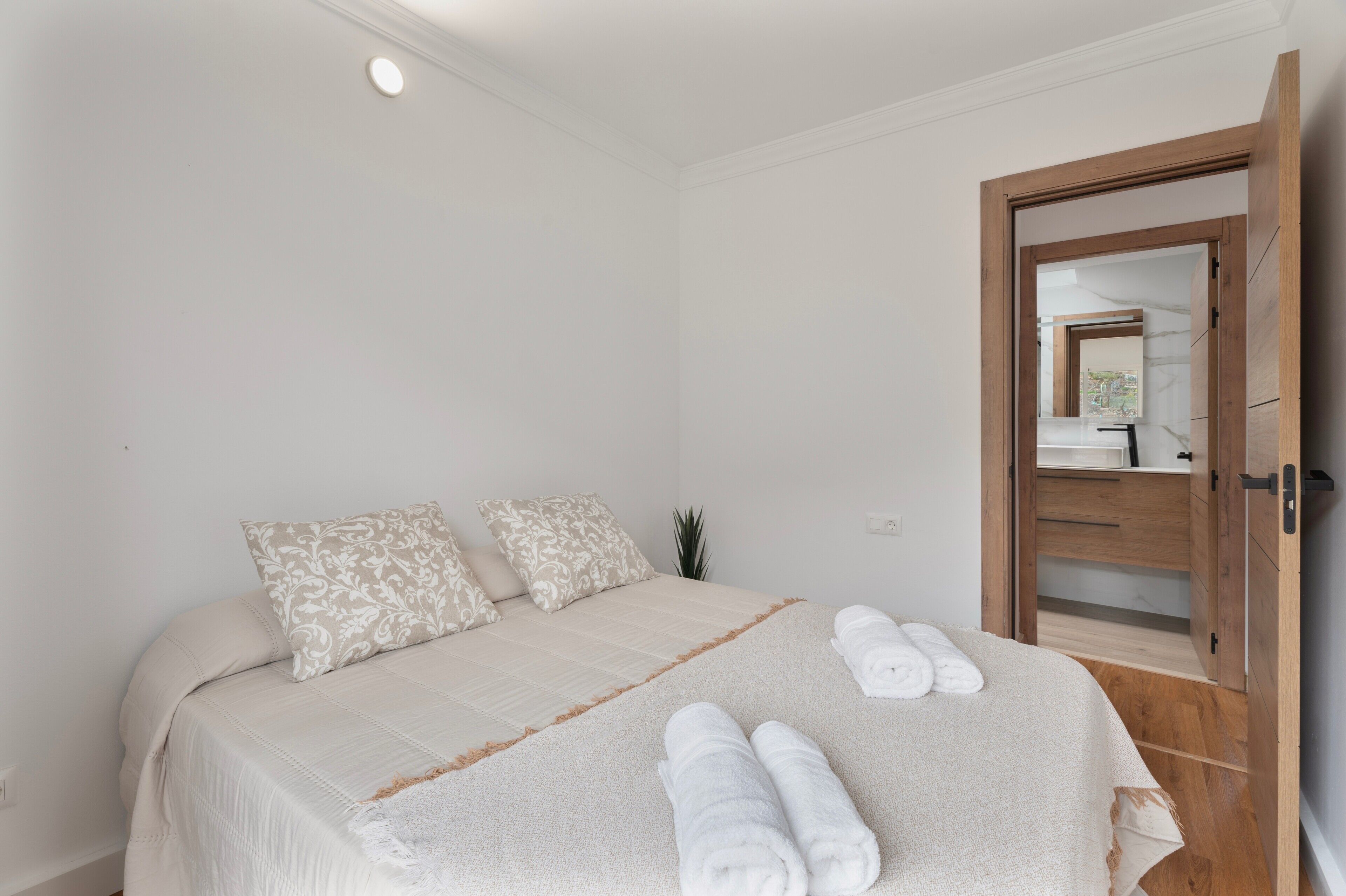 A bedroom with a bed, pillows, a wooden door, and a mirror.