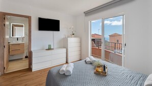 A bedroom with a bed, a TV, a dresser, a mirror, a window, and a balcony.
