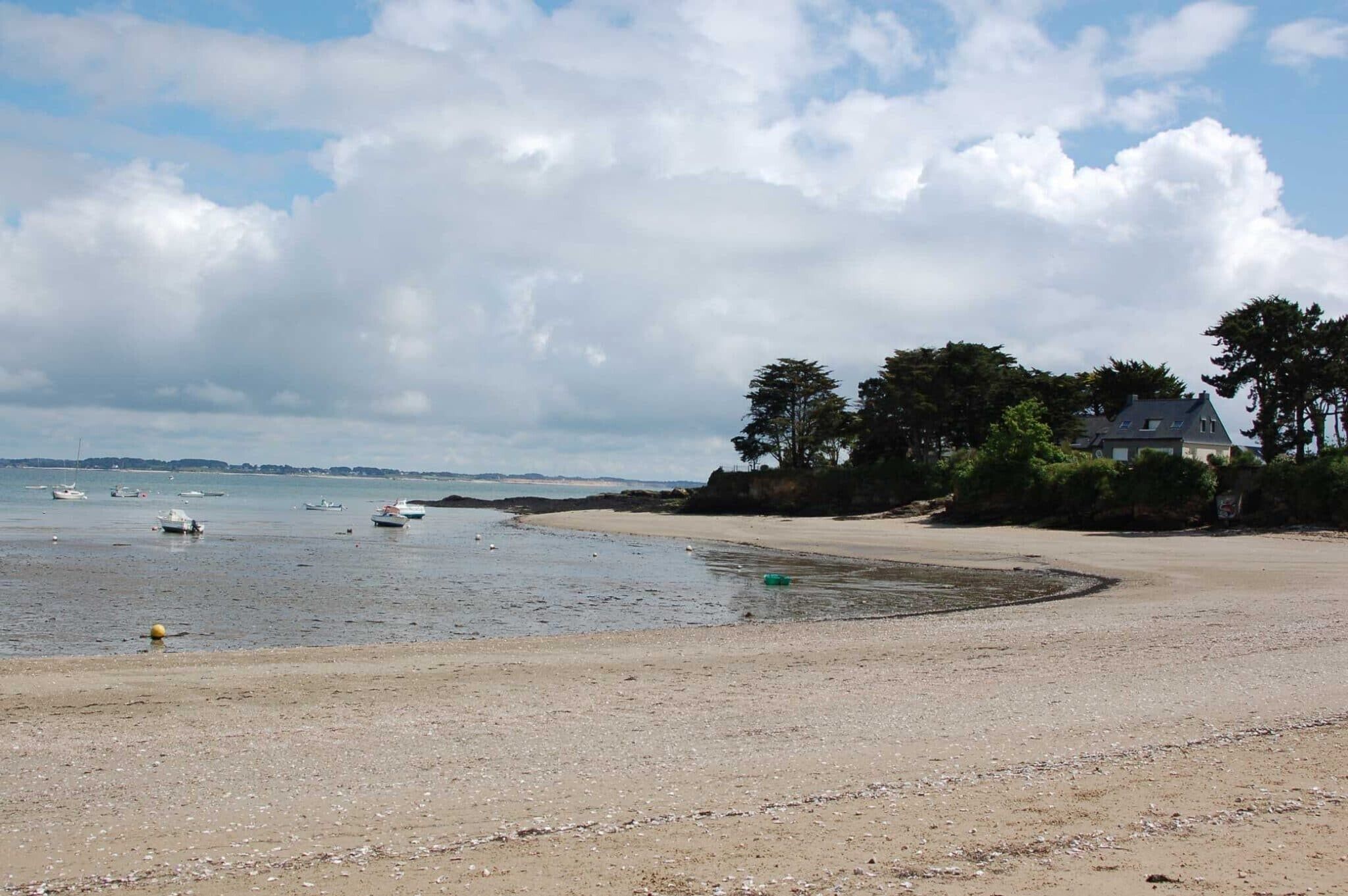 Une plage avec des bateaux, un rivage sablonneux et une maison entourée d’arbres.