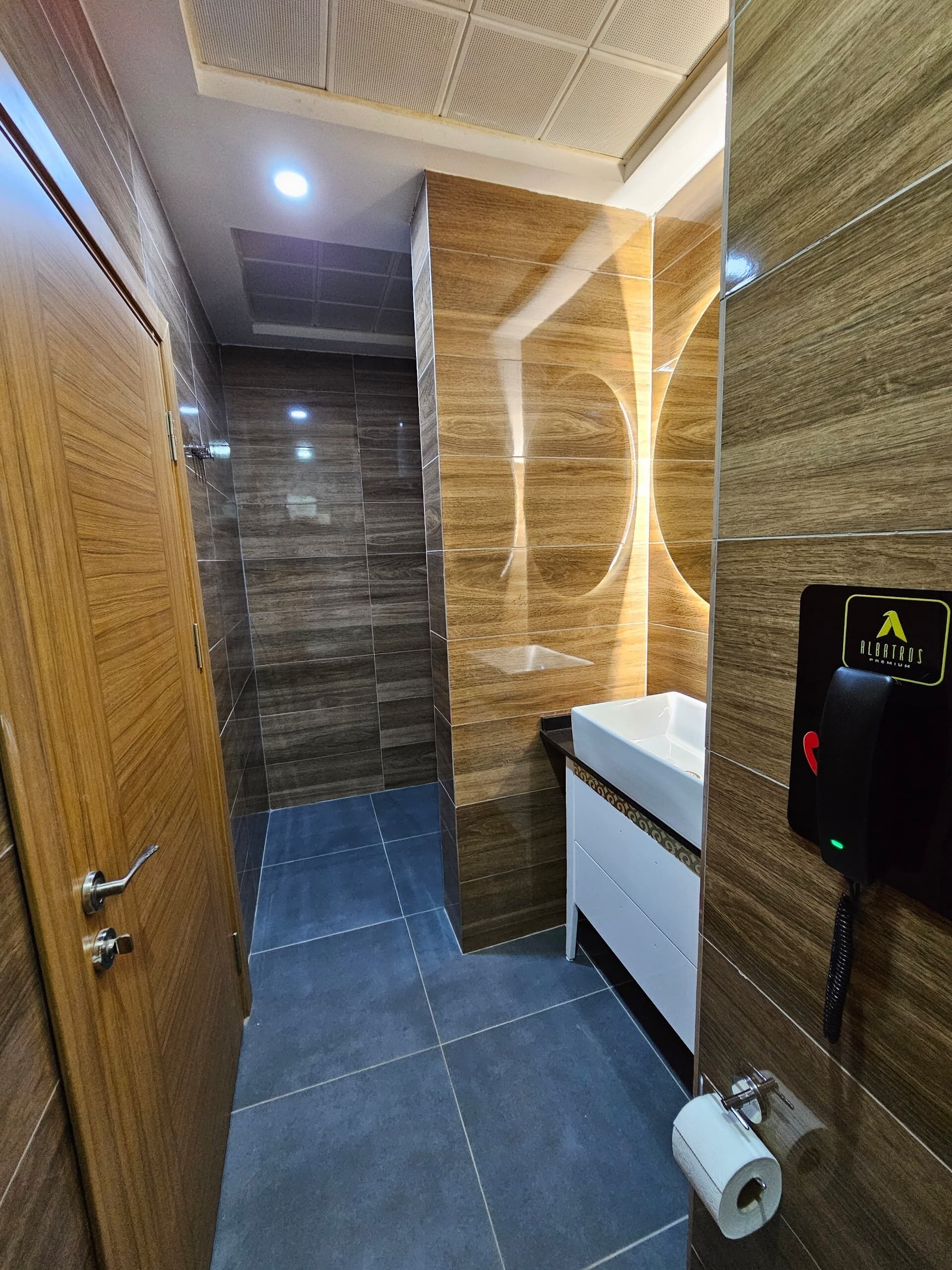 A modern bathroom with a wooden door, a sink with a mirror, and a toilet.