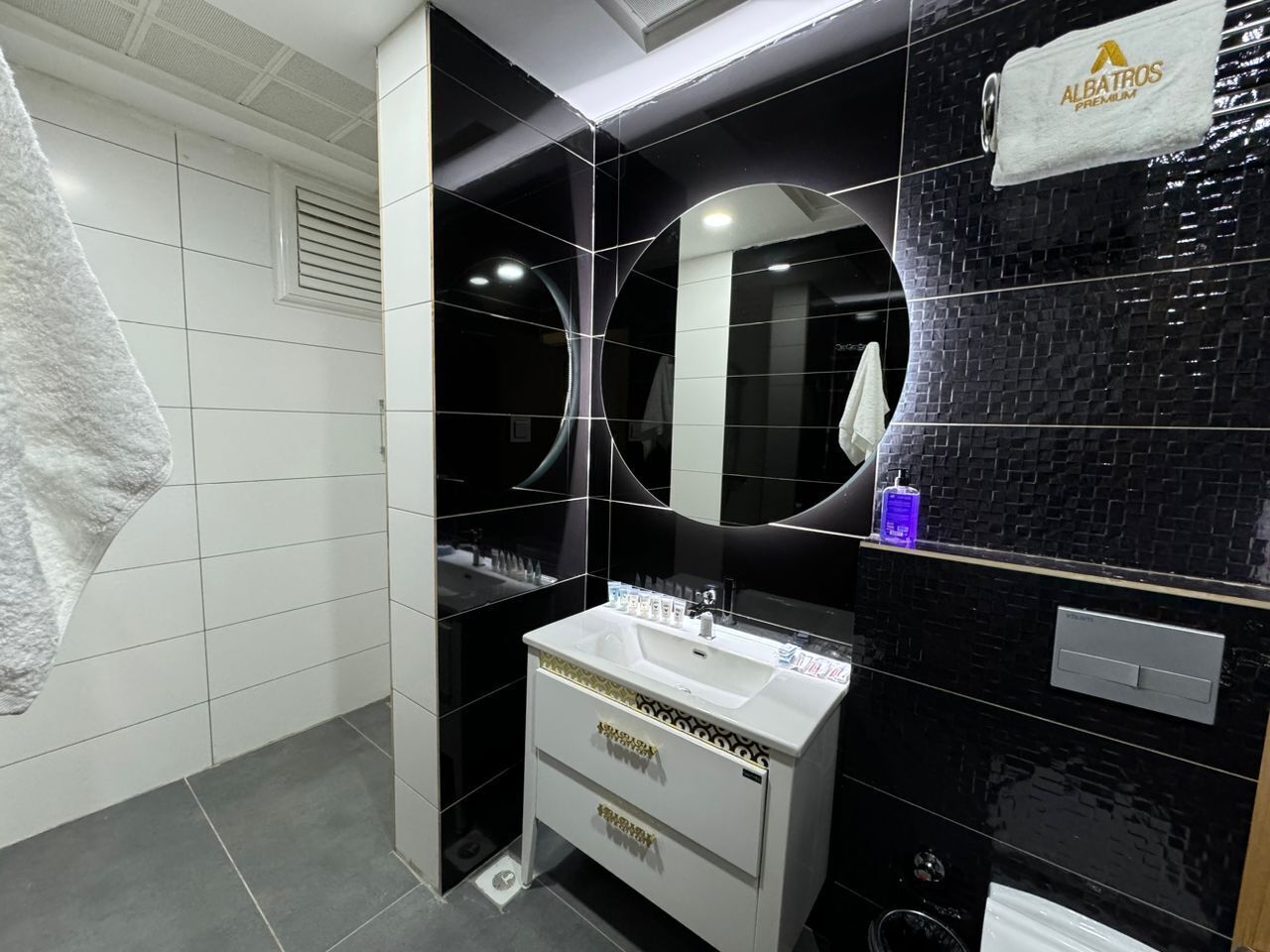 Un baño moderno con tocador blanco, paredes de azulejos negros y un espejo sobre el lavabo.