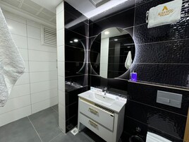 Un baño moderno con tocador blanco, paredes de azulejos negros y un espejo sobre el lavabo.