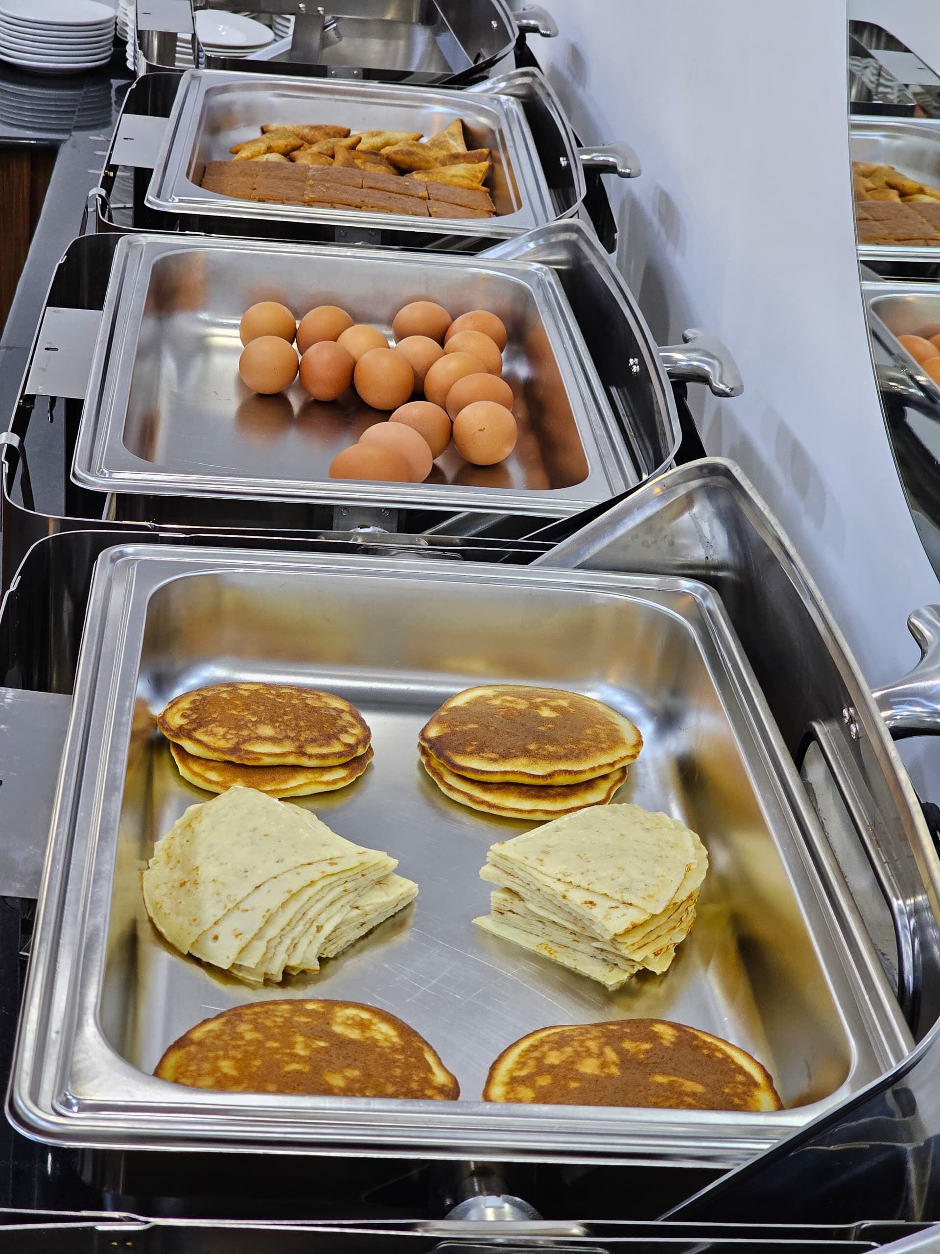 Buffet com diversos alimentos, incluindo ovos, panquecas e batatas fritas.