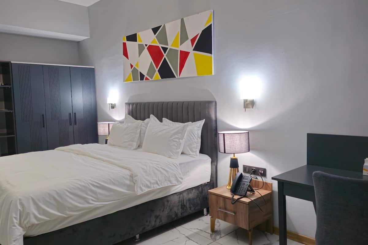 A modern hotel room with a large bed, bedside tables, a desk, and a wardrobe.