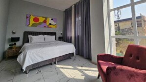 A bedroom with a bed, a red chair, a painting, and a large window. - Albatros Premium Hôtel (Yaoundé)