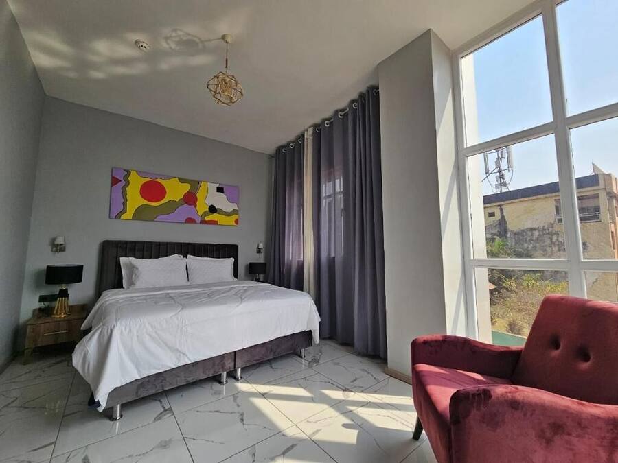 Une chambre à coucher avec un lit, une chaise rouge, un tableau et une grande fenêtre.