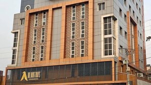 A multi-story building with a modern architectural design, featuring a prominent glass section on the upper floor and a facade with a mix of brick and glass materials. - Albatros Premium Hôtel (Yaoundé)