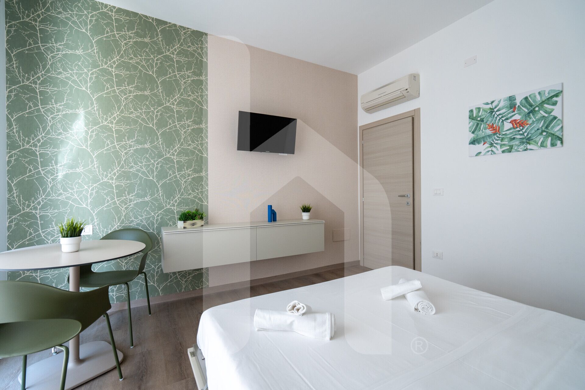 Una camera d'albergo moderna con un letto, una scrivania, una sedia, una televisione e la porta del bagno.